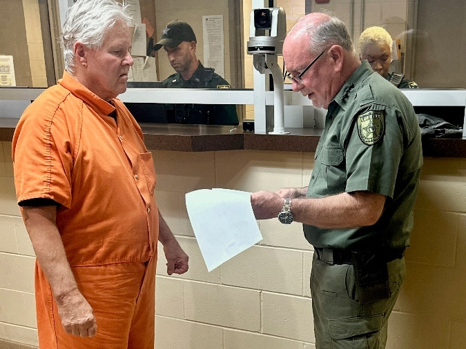 Flagler County Sheriff Rick Staly, right, reads the arrest warrant for Kermit Booth at the Sheriff Perry Hall Inmate Detention Facility in Bunnell, Fla., on Friday, Sept. 5, 2025.